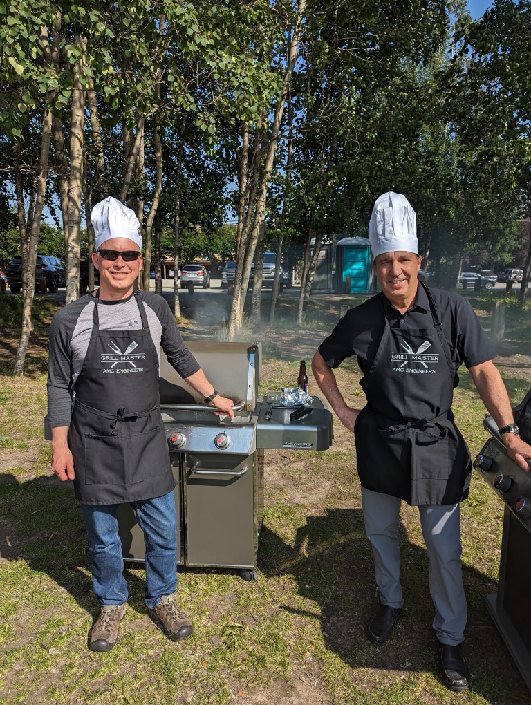 Dave Shumway and Ken Ratcliffe grilling and wearing Grill Master aprons and chefs hats
