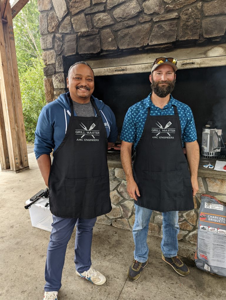 John and another AMC employee wearing aprons that say Grill Master AMC Engineers