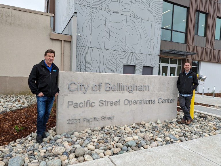 Two AMC employees standing in front of billboard for the City of Bellingham Pacific Street Operations Center