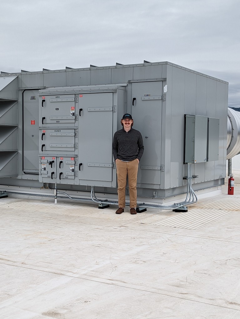 Man standing in front of large machinery on a rooftop
