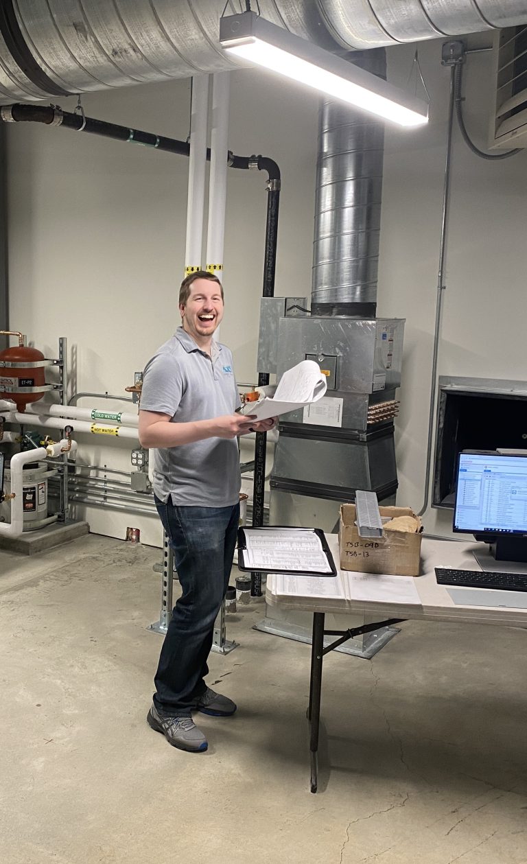 Christian holding papers in front of machinery and pipes