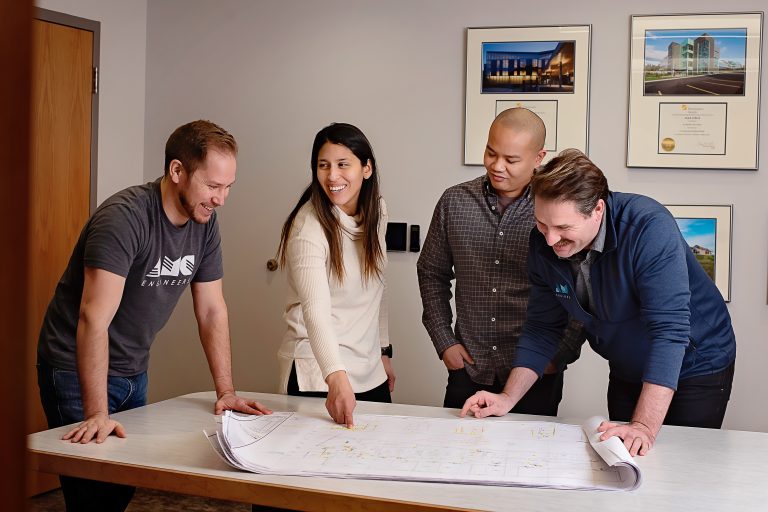 Four AMC employees looking at blueprints on a table