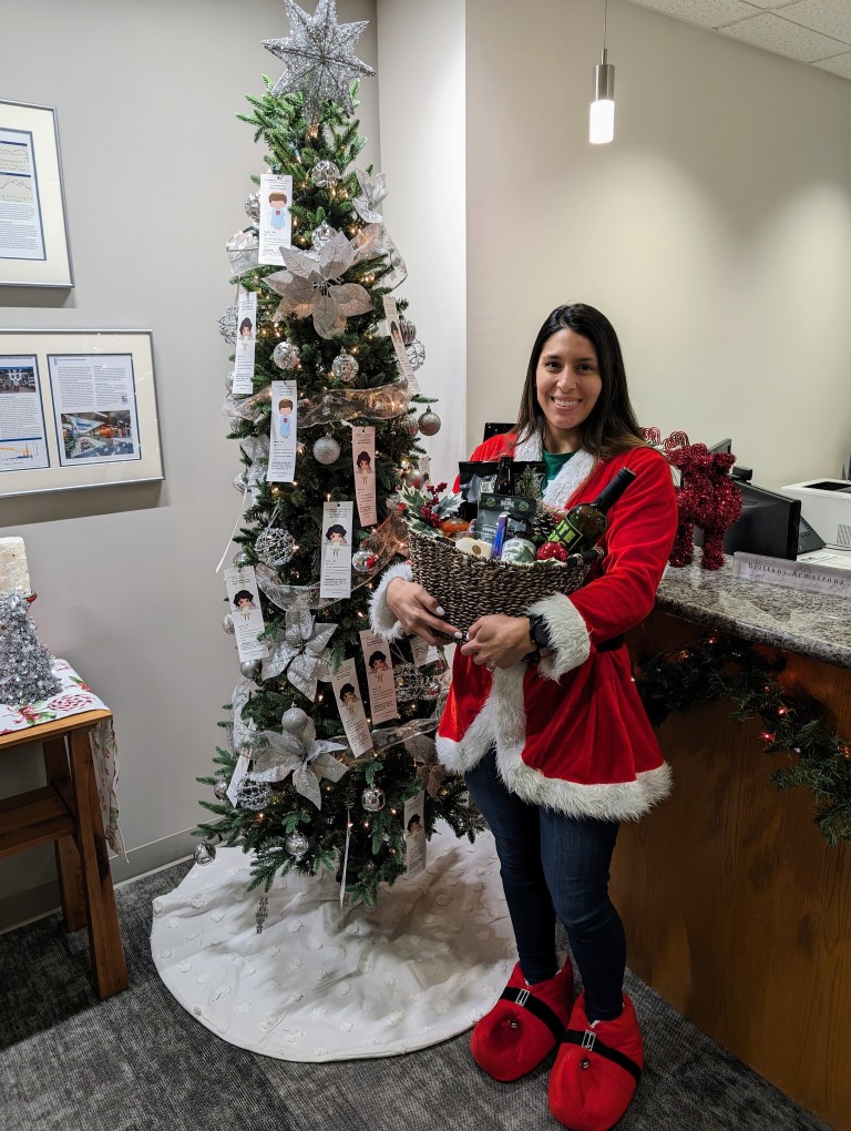 Deborah holding a gift basket in front of a Christmas tree