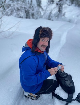 Drew holding a camera on a snowy mountainside