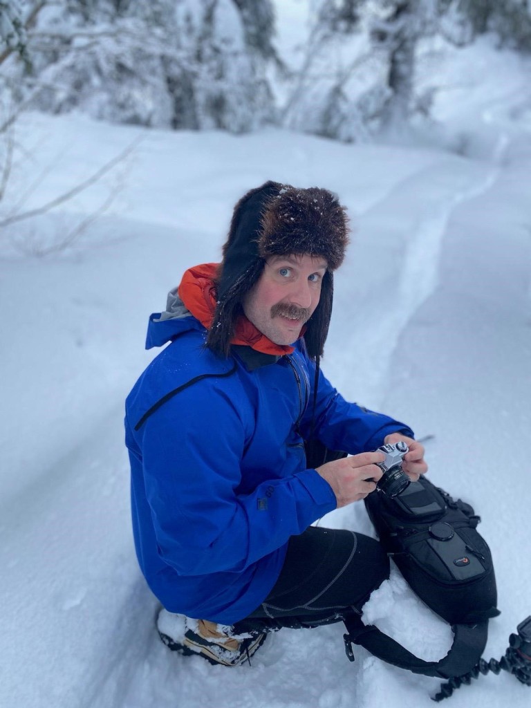 Drew holding a camera on a snowy mountainside