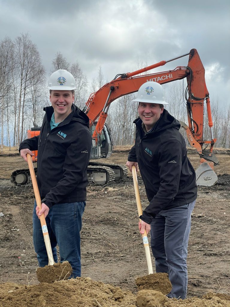 Two men in hard hats digging in front of an excavator