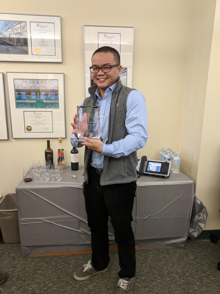 Edsel standing at an office celebration holding an award