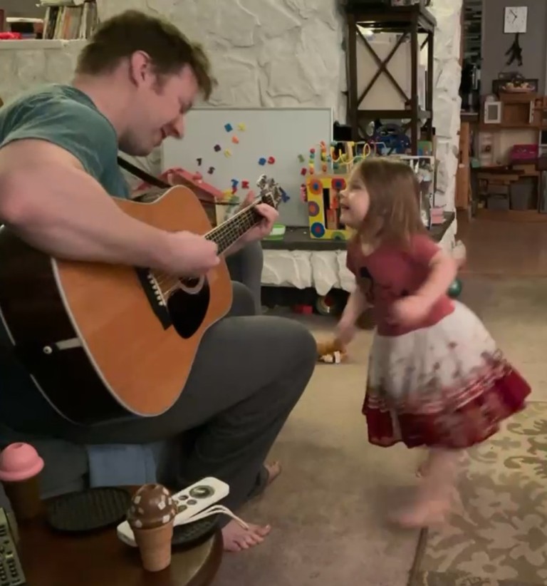 Tyler Tremont playing guitar with a young girl dancing