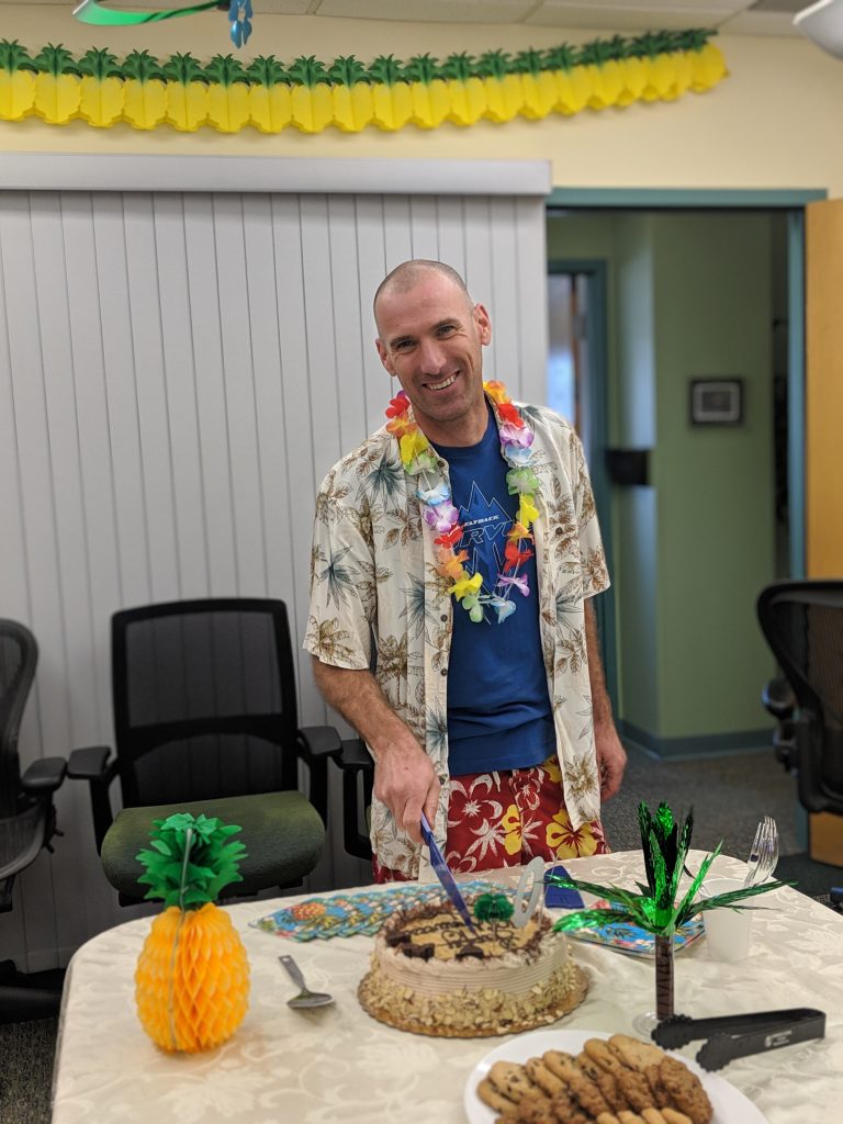 John in tropical clothing at office party cutting a cake