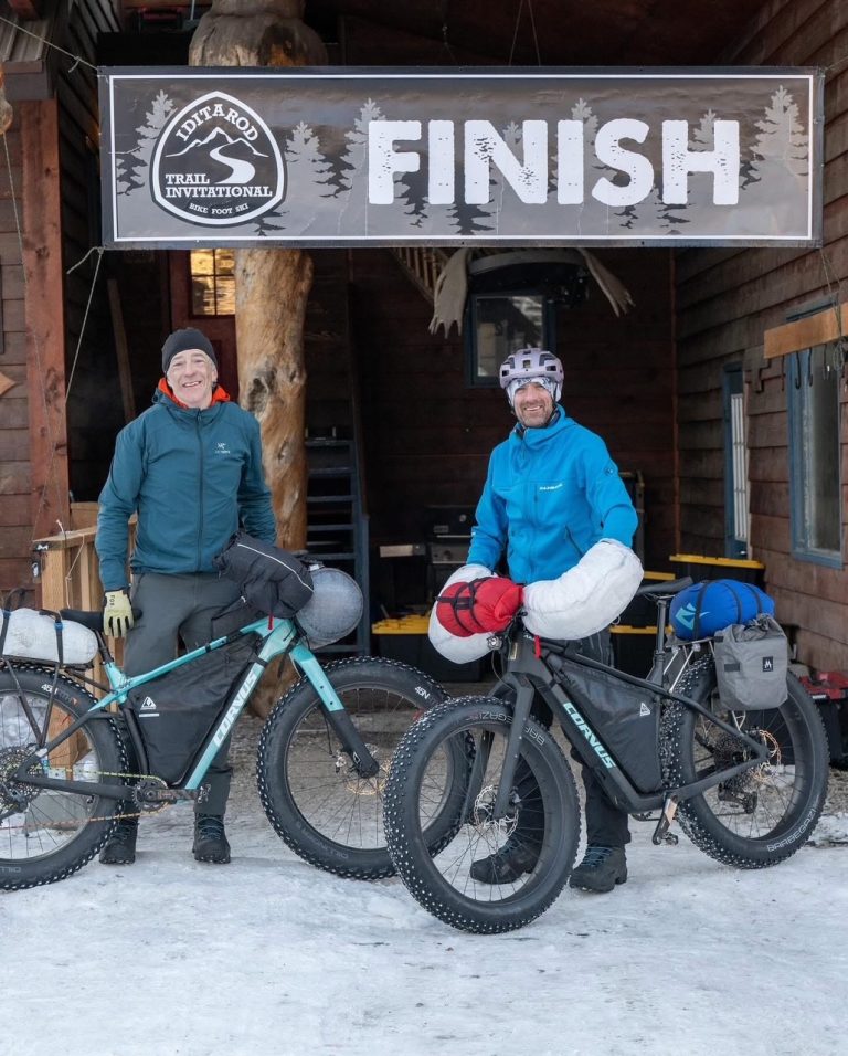 John with his bike and the finish line of the Iditarod trail invitational