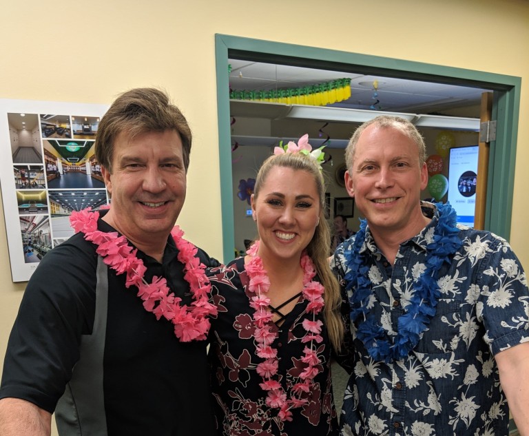 Michelle Pasion standing with two other AMC employees in tropical clothing at an office party