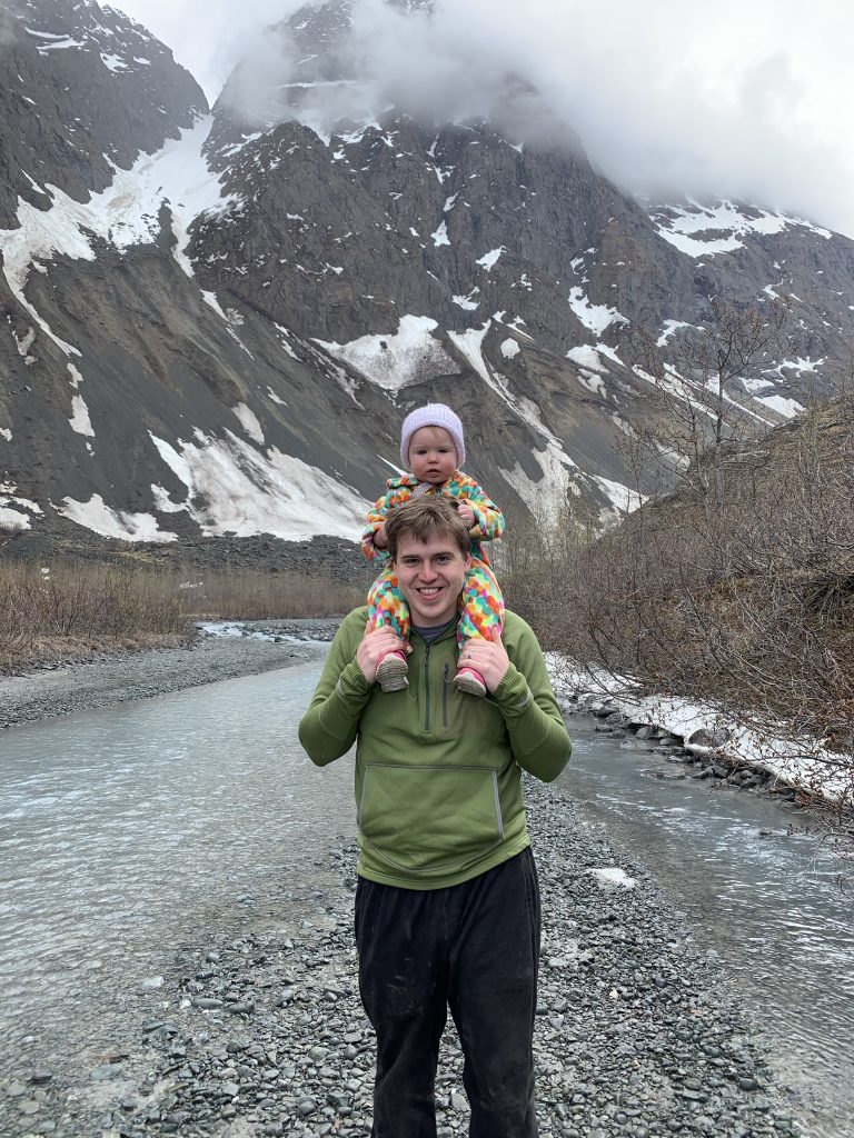 A baby sitting on Trentons shoulder in front of mountains