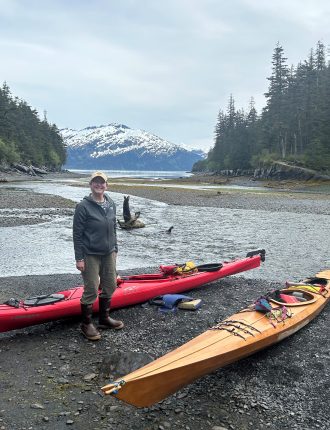 Tami near a kayak on a wooded coast