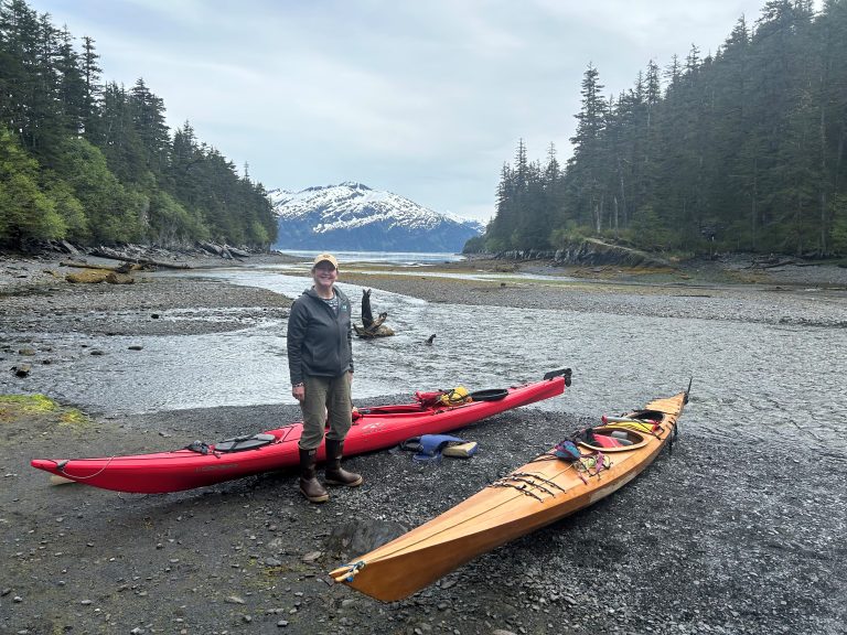 Tami near a kayak on a wooded coast