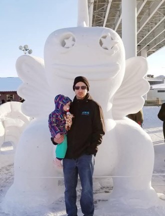 Man posing in front of snow sculpture with toddler in his arms