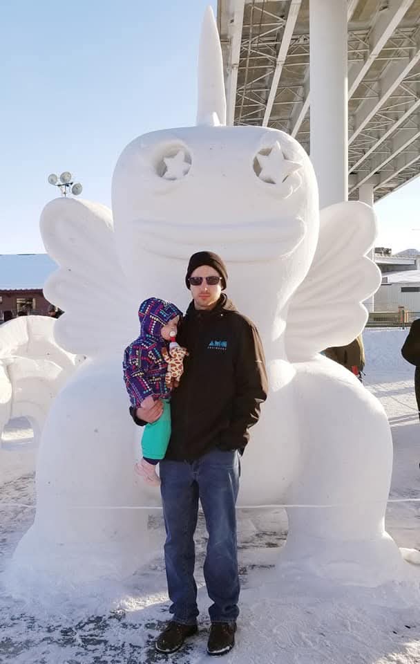 Man posing in front of snow sculpture with toddler in his arms