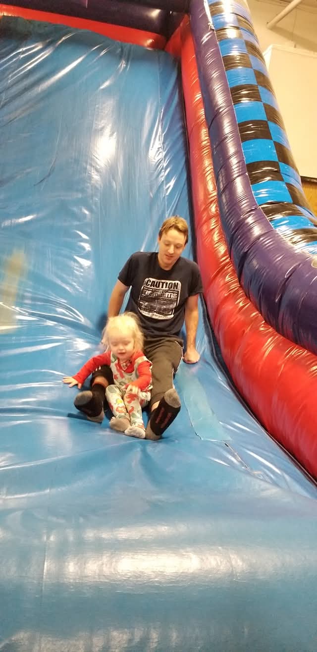 Man sliding down inflatable slide with a young girl