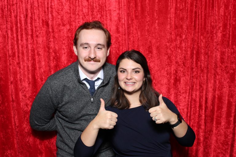 Kyle with a woman at a Christmas party standing in front of red velvet backdrop