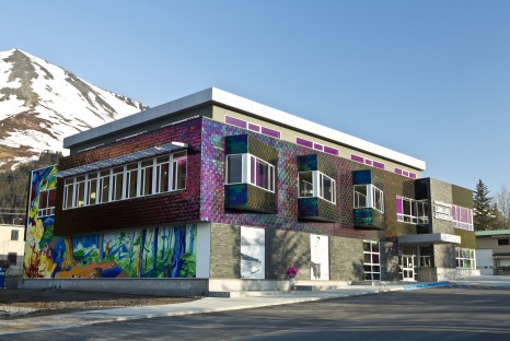 Iridescent tiled and stone brick exterior of multistory building with colorful mural of forest