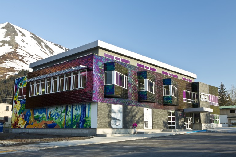 Iridescent tiled and stone brick exterior of multistory building with colorful mural of forest
