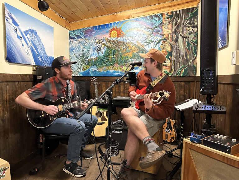 Two men in small studio space playing guitars