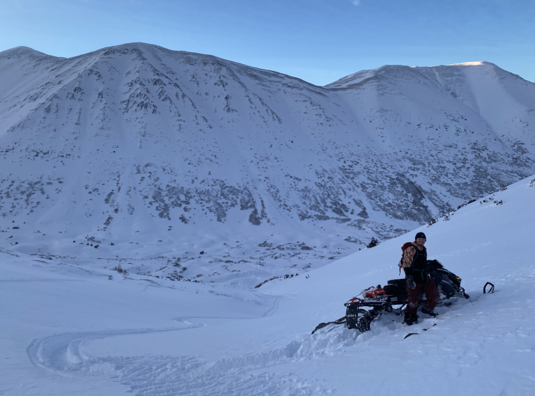 Jack Shumacher on snowmobile beside a snowy mountain