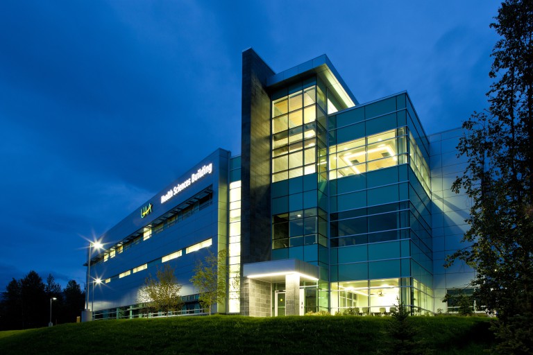 Exterior of multistory building with large glass windows and tiled walls lit at night