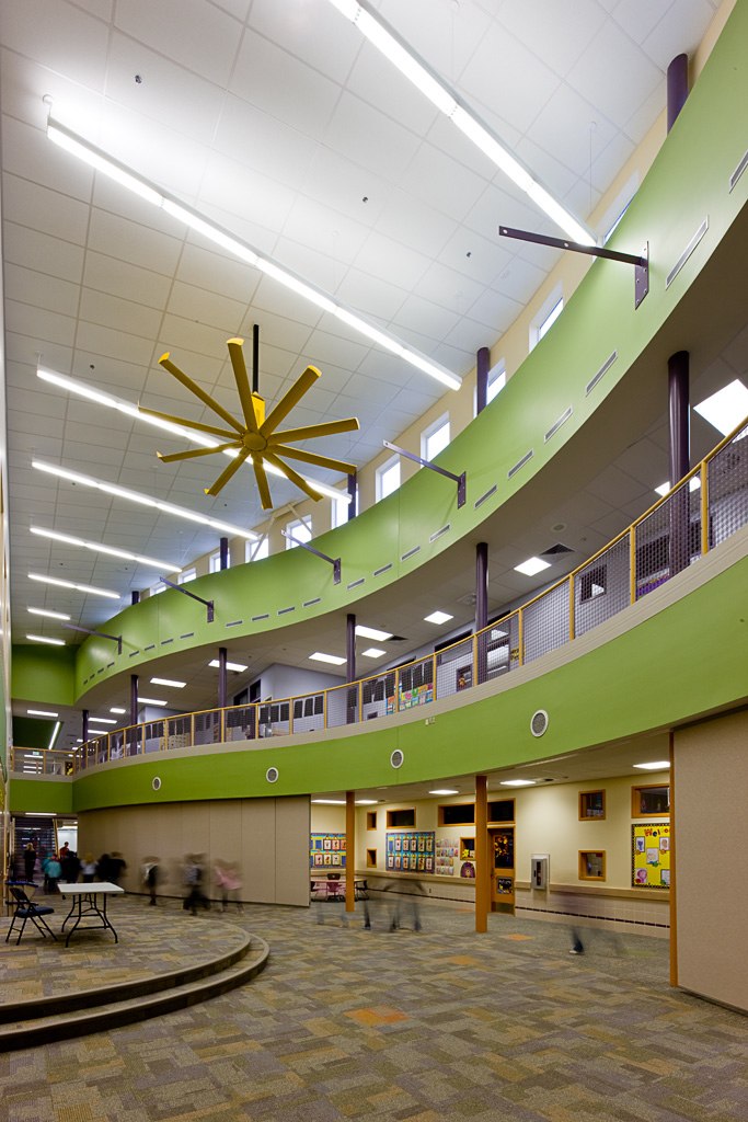Multistory interior with high ceilings, large decorative fan, balconies, and colorful green walls in elementary