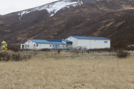 White slab building with bright blue roof beside snowy mountains