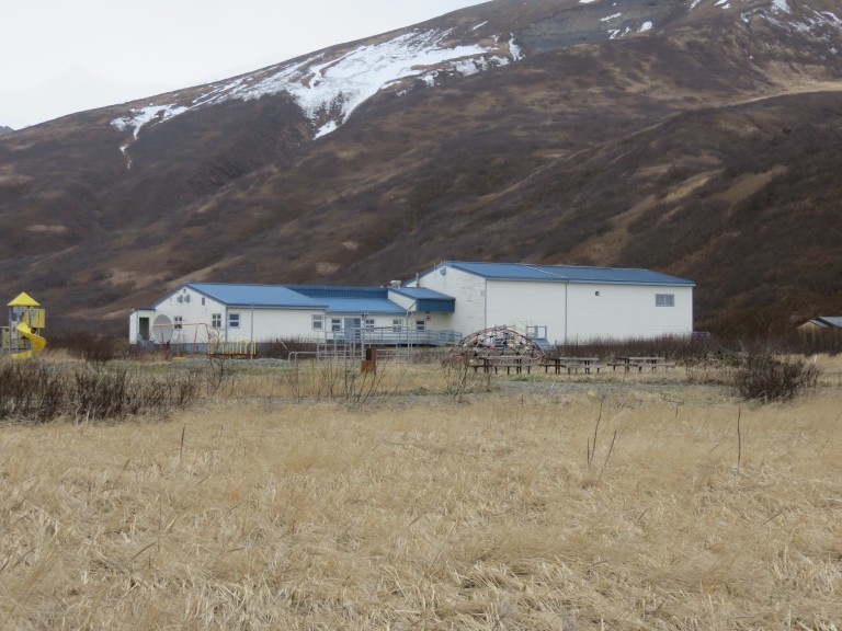 White slab building with bright blue roof beside snowy mountains