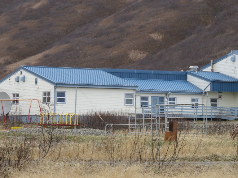 White slab building with bright blue roof beside snowy mountains