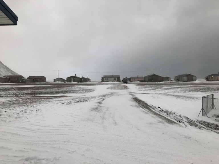 Multiple small wooden buildings in snowy flat terrain