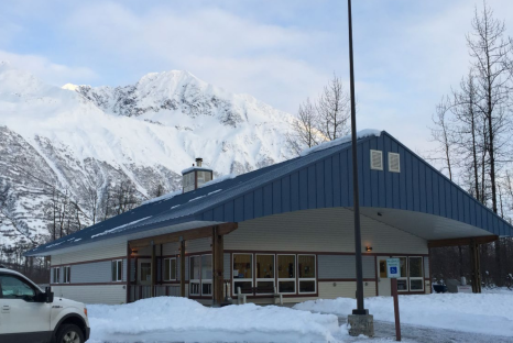 Tan slab one story building with bright blue roof in Alaskan mountains
