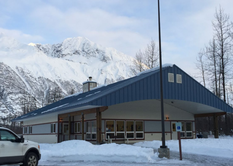 Tan slab one story building with bright blue roof in Alaskan mountains